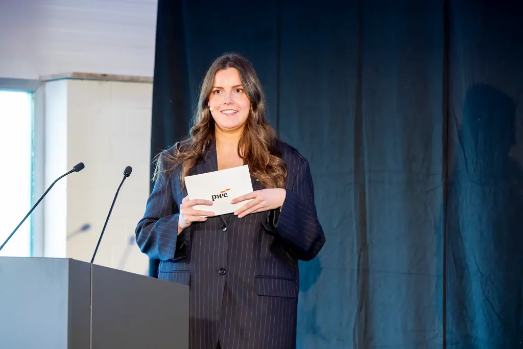 Rednerin steht auf Bühne mit PwC-Moderationskarte